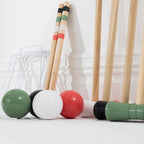 A set of croquet mallets and balls arranged on a white surface against a white paneled wall. 