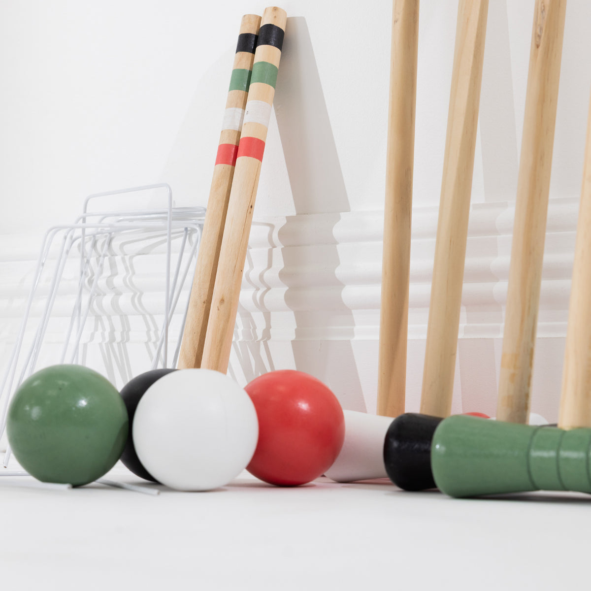 A set of croquet mallets and balls arranged on a white surface against a white paneled wall. 