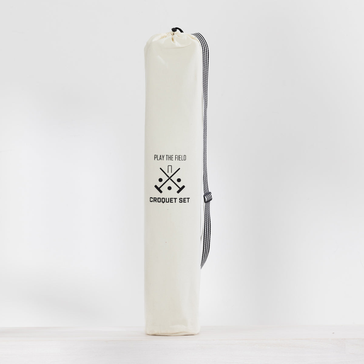 An canvas croquet set bag with a black drawstring closure and a black-and-white striped carrying strap