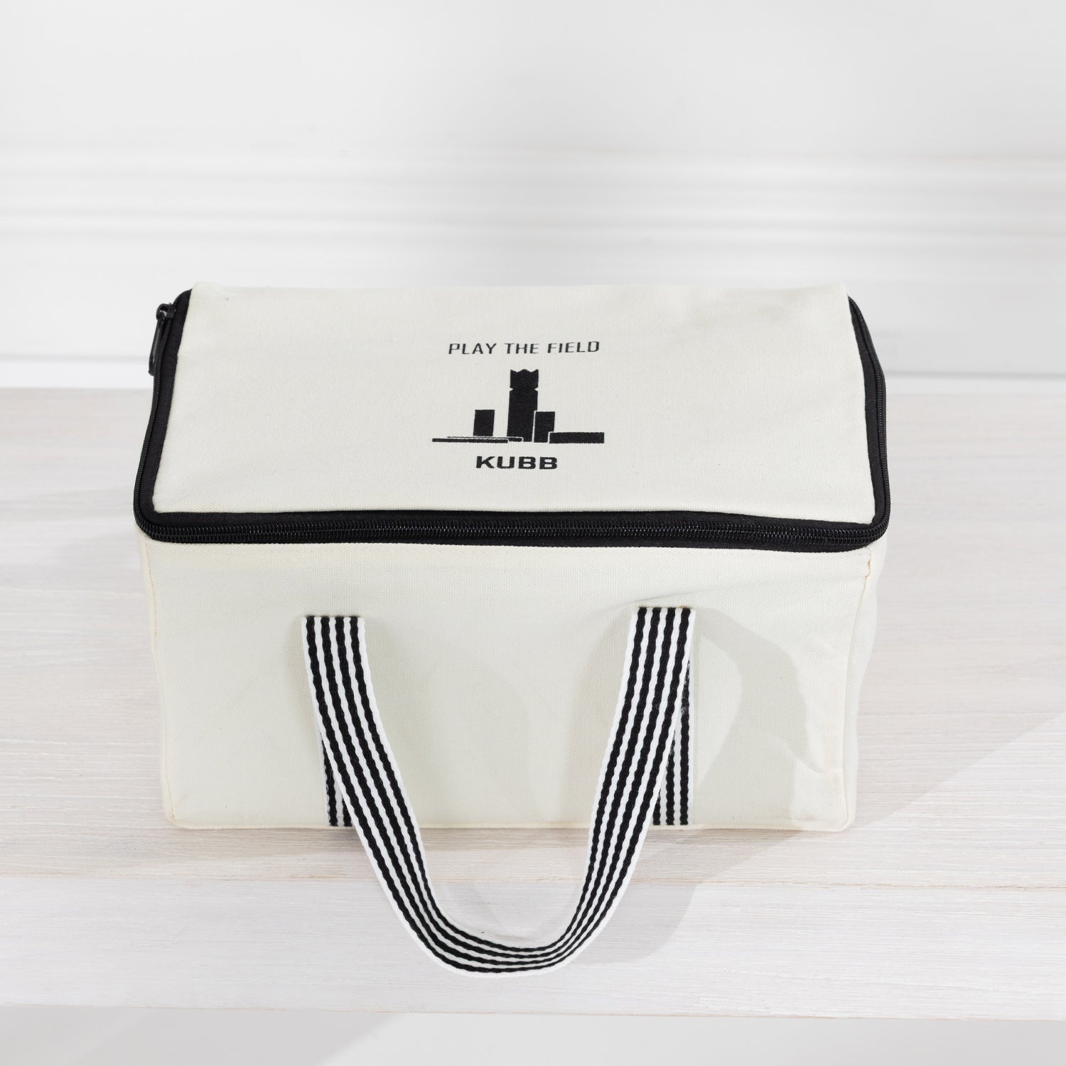 The outdoor game Kubb in a canvas bag with black trim, black-and-white striped handles.