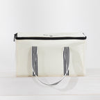 The outdoor game Kubb in a canvas bag with black trim, black-and-white striped handles.