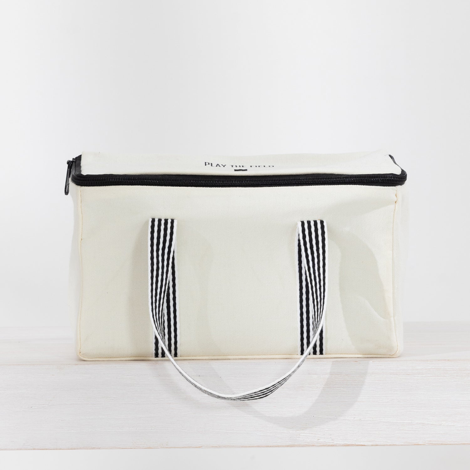 The outdoor game Kubb in a canvas bag with black trim, black-and-white striped handles.
