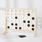 A wooden Connect-four in a row game with a light natural wood frame and black-and-white circular tokens, photographed on a clean white floor against a white wall.