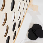 A close up of a wooden Connect-four in a row game with a light natural wood frame and black-and-white circular tokens, photographed on a clean white floor.