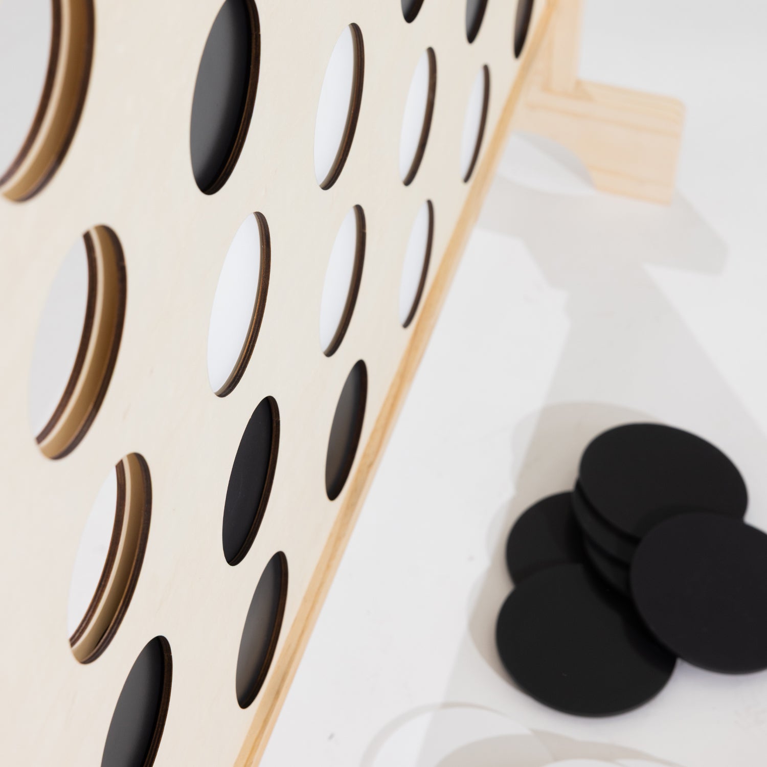 A close up of a wooden Connect-four in a row game with a light natural wood frame and black-and-white circular tokens, photographed on a clean white floor.