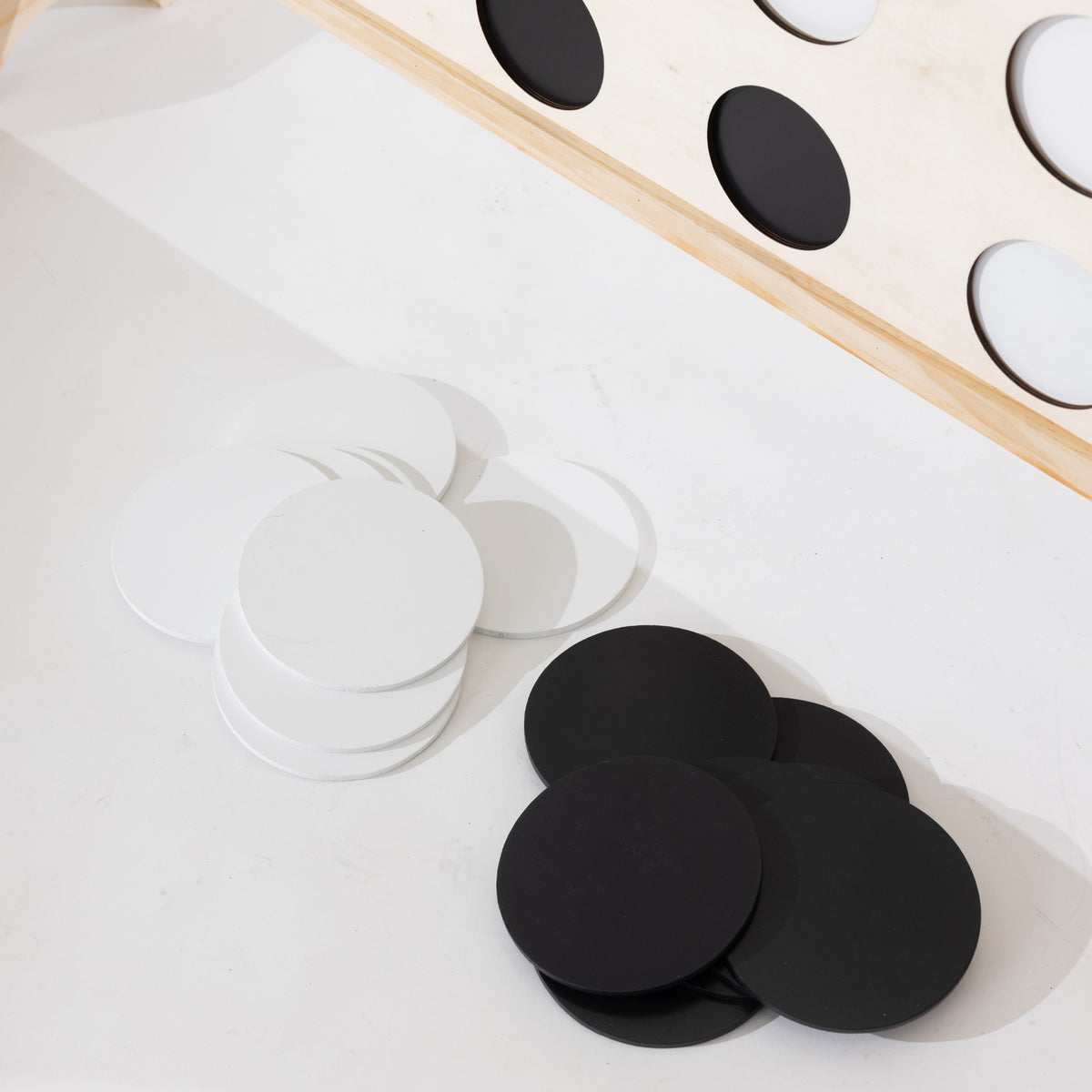 White and black round wooden discs arranged on a white surface, with a partial light wood board visible in the upper right containing circular cutouts.