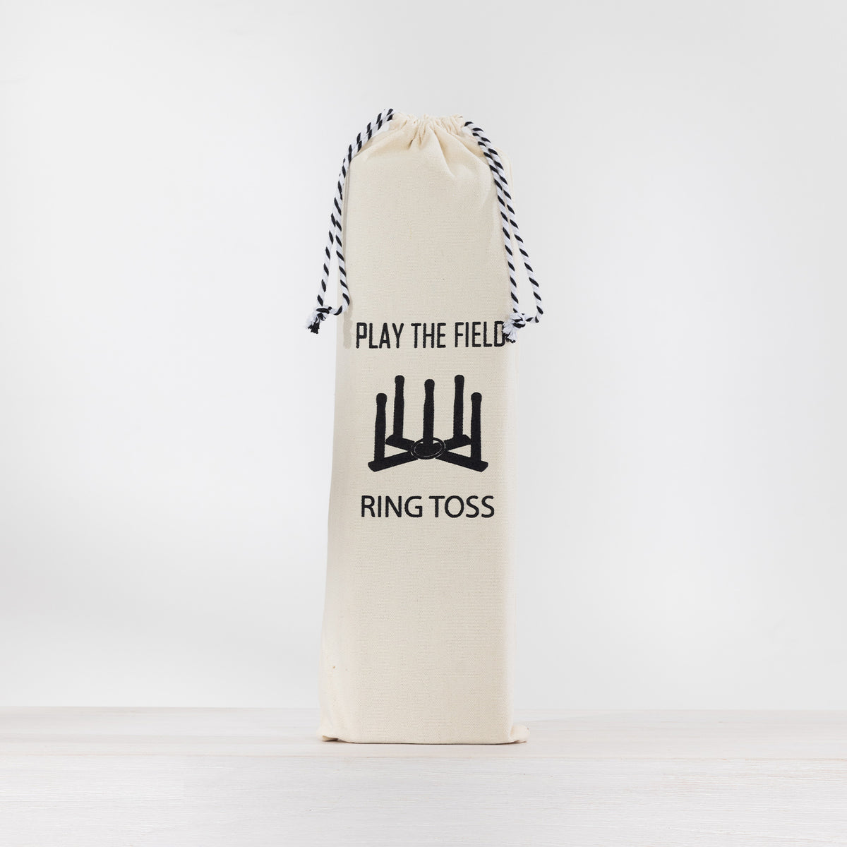 Cream drawstring storage bag for the Play the Field Ring Toss game, featuring black printed branding and a ring toss illustration.