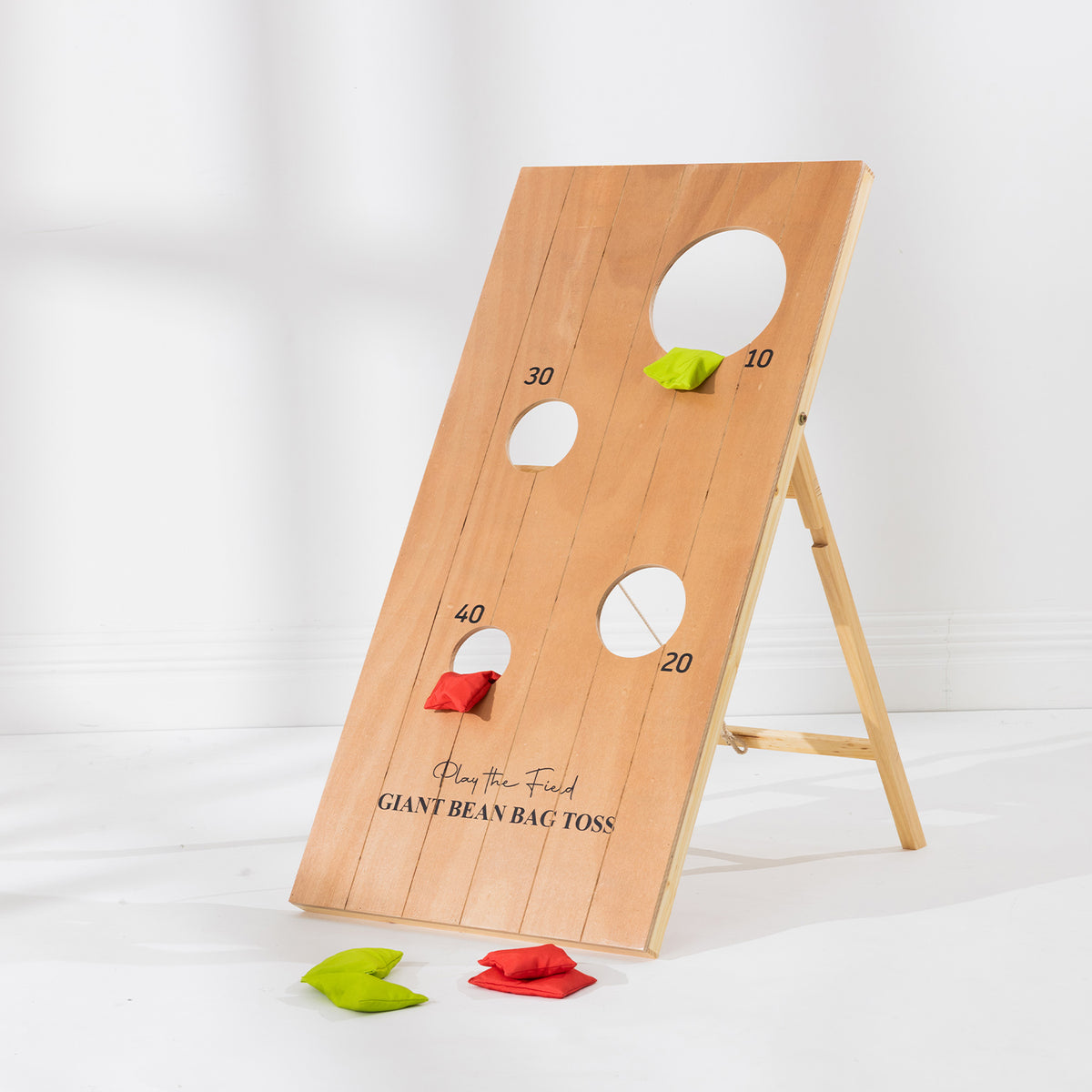 Play the Field Giant Bean Bag Toss board set up on its wooden stand with red and green bean bags ready for play.