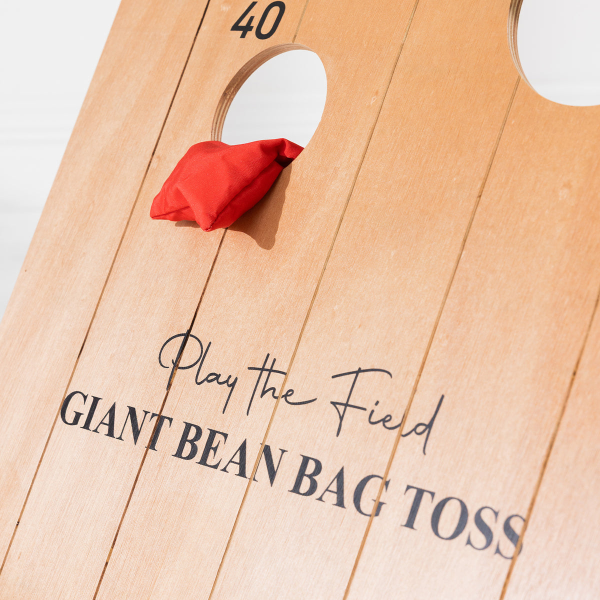 Close-up of the wooden Play the Field Giant Bean Bag Toss board with a red bean bag beside the 40-point scoring hole.