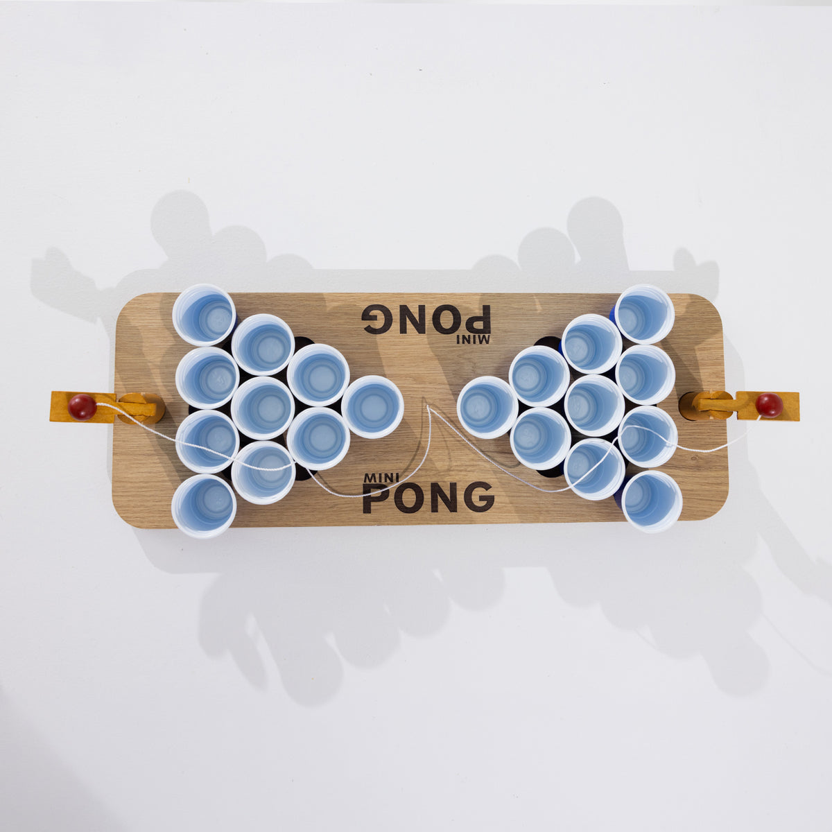 Overhead view of the Play the Field Mini Pong wooden game board with blue cups and ball launchers at each end.