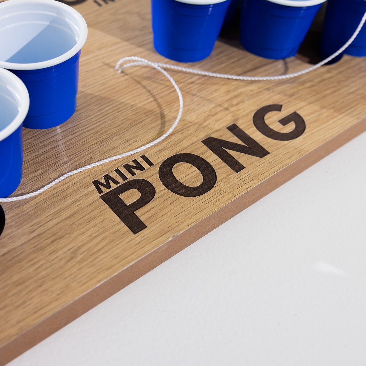 Close-up of the Play the Field Mini Pong logo on the wooden game board with blue cups and a white tether cord.