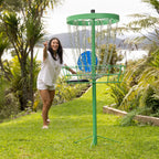 Woman playing Play the Field Disc Golf outdoors, with a blue disc landing in the green chain target.