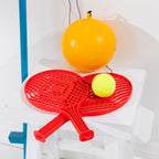 Close-up of two red racquets, a yellow tennis ball and orange tetherball included with the game.