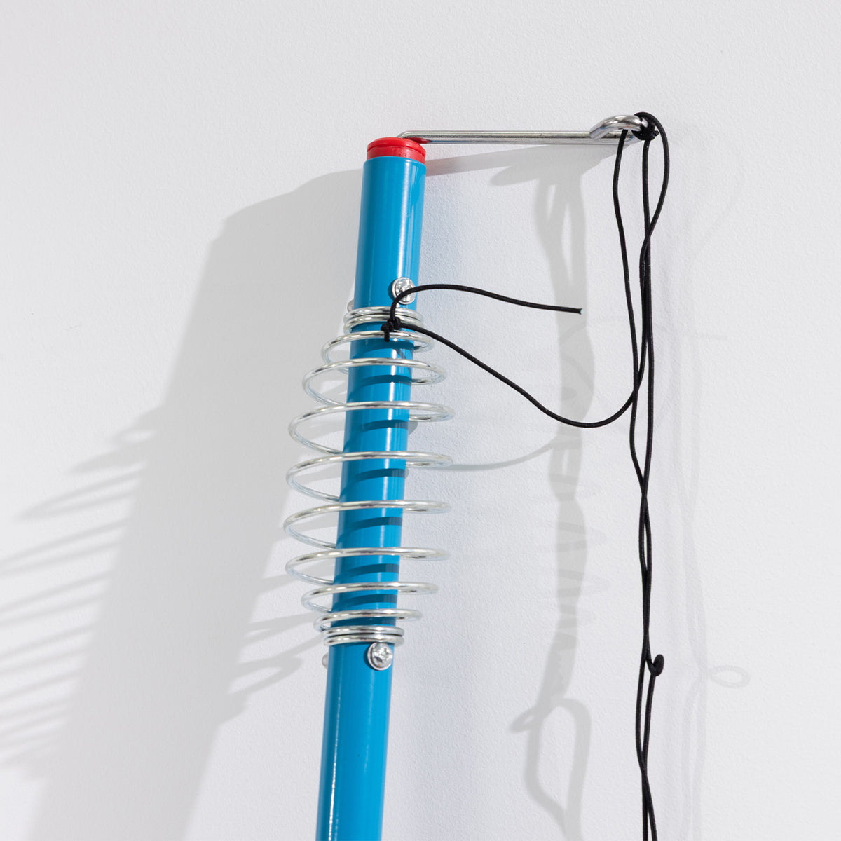 Close-up of the blue tetherball pole with metal spring attachment and black tether cords.