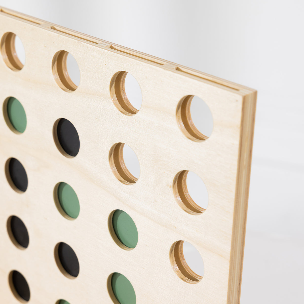 Close-up of the Play the Field 4-In-A-Row wooden board showing the circular grid and green and black playing coins.