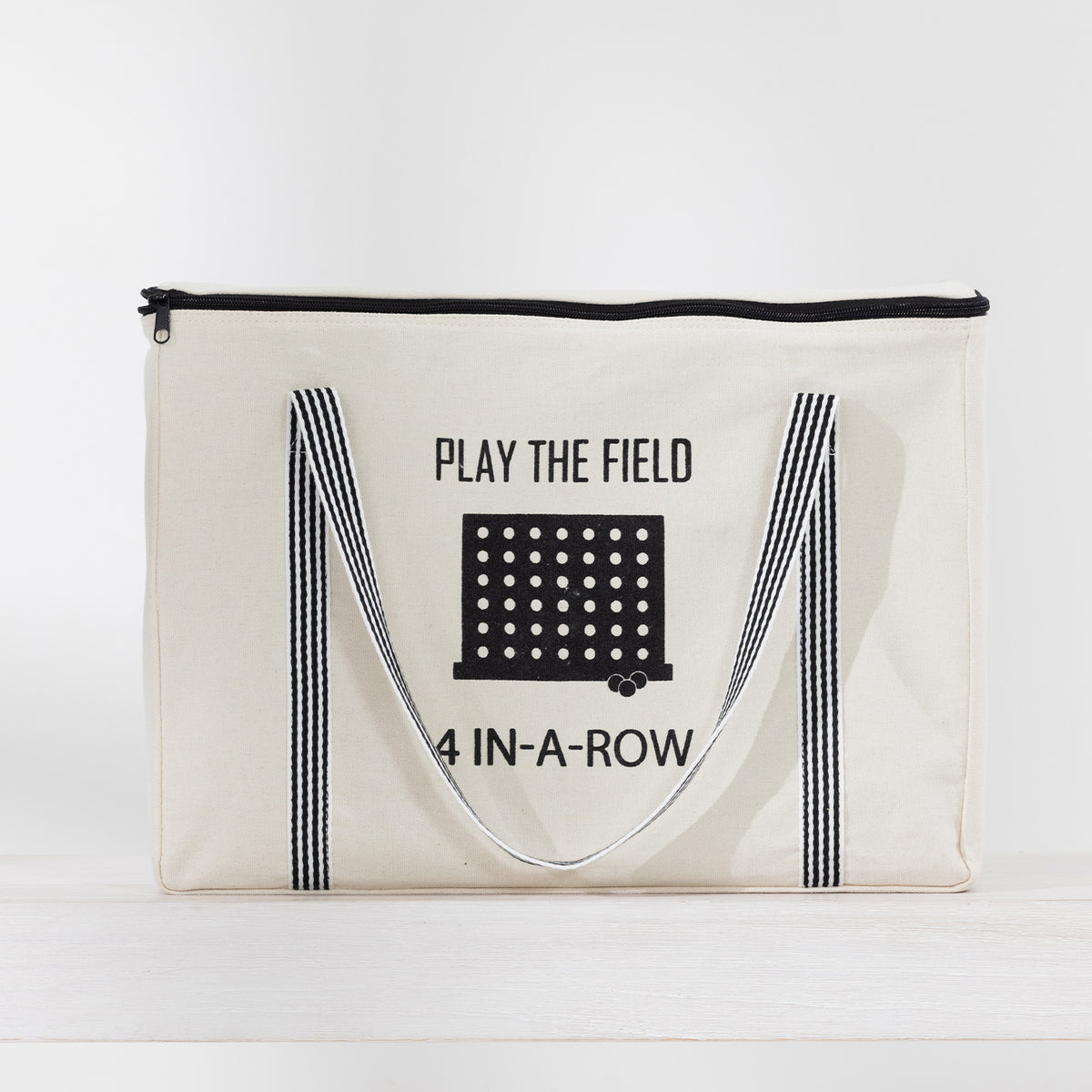 Play the Field 4-In-A-Row cream storage bag with black striped handles and printed game design.
