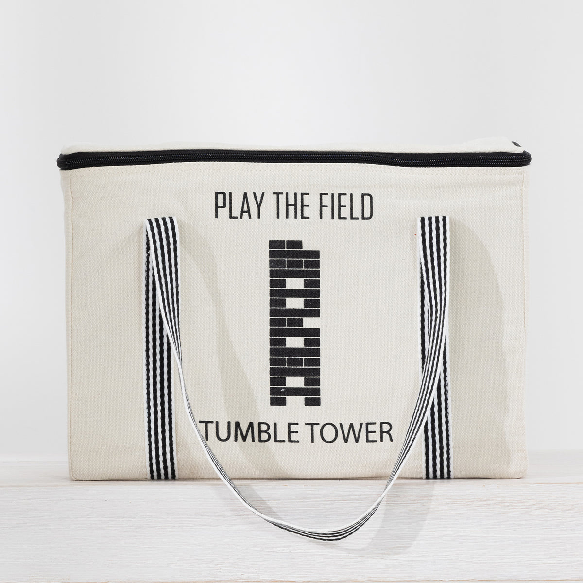 Play the Field Tumble Tower cream storage bag with black striped handles and printed tower design.