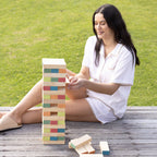 Woman playing Play the Field Tumble Tower outdoors, carefully removing a wooden block from the stacked tower.