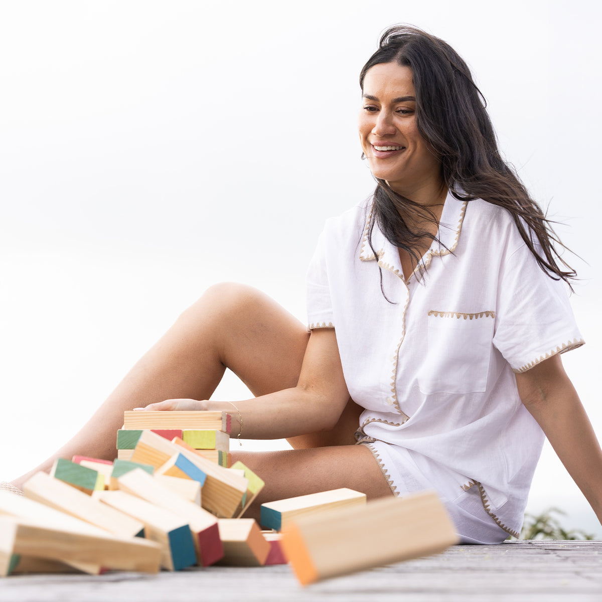 Play the Field Tumble Tower game with a woman sitting outdoors beside the fallen colourful wooden blocks.
