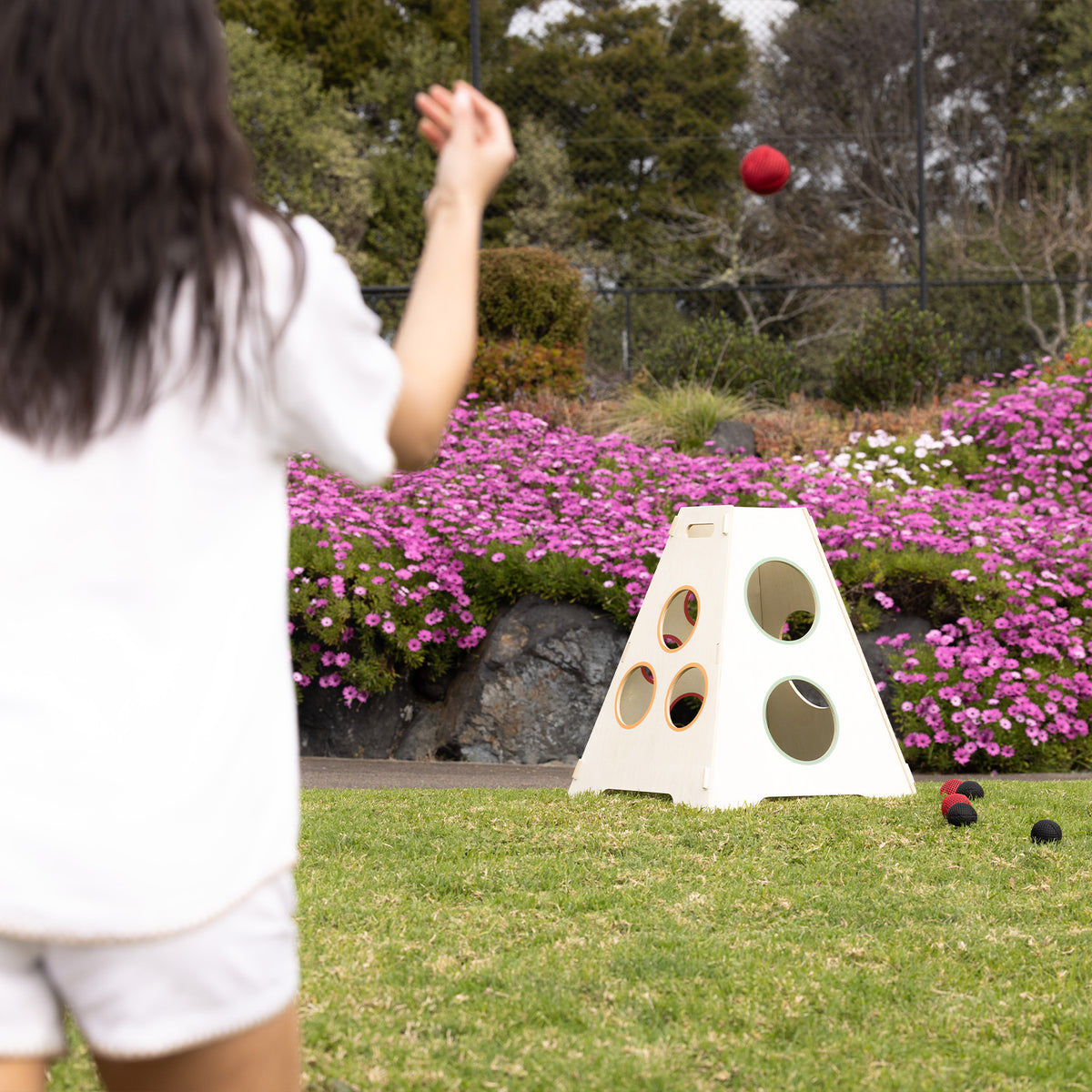 Woman throwing a red ball towards the Play the Field Tower Ball game outdoors on a lawn.