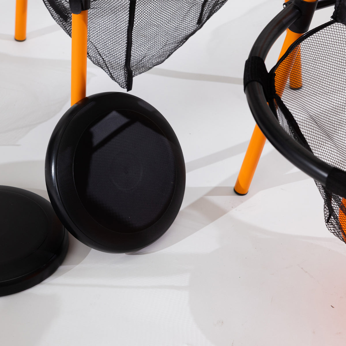 Close-up of the black flying discs beside the orange frame and mesh target.