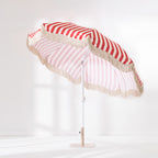 Red and white striped patio umbrella with cream tassel edging shown open from an angled side view.