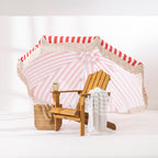 Red and white striped patio umbrella with cream tassel edging styled with a wooden outdoor chair and woven beach bag.
