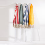 Four closed patio umbrellas in red stripe, sage green, blue stripe and yellow designs with cream tassel edging.