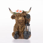A Highland cow figurine with long brown hair, holding a black lantern and wearing a flower crown, photographed on a white background.