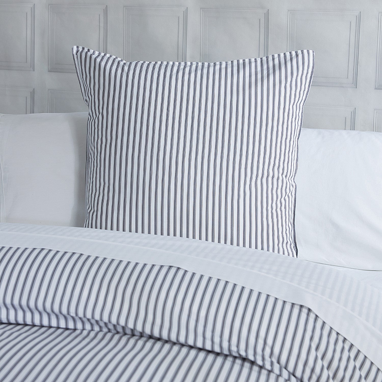 Striped bed sheets and pillowcases on a bed with a gray headboard.