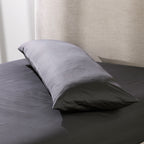 A charcoal body pillow is dressed in a smooth cotton pillowcase and styled on a neatly made bed, showcasing its clean, luxurious finish and full-length comfort.