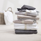 A stack of premium sheets in timeless neutral tones is neatly folded and finished with elegant storage bands, creating a refined and organised linen cupboard aesthetic.