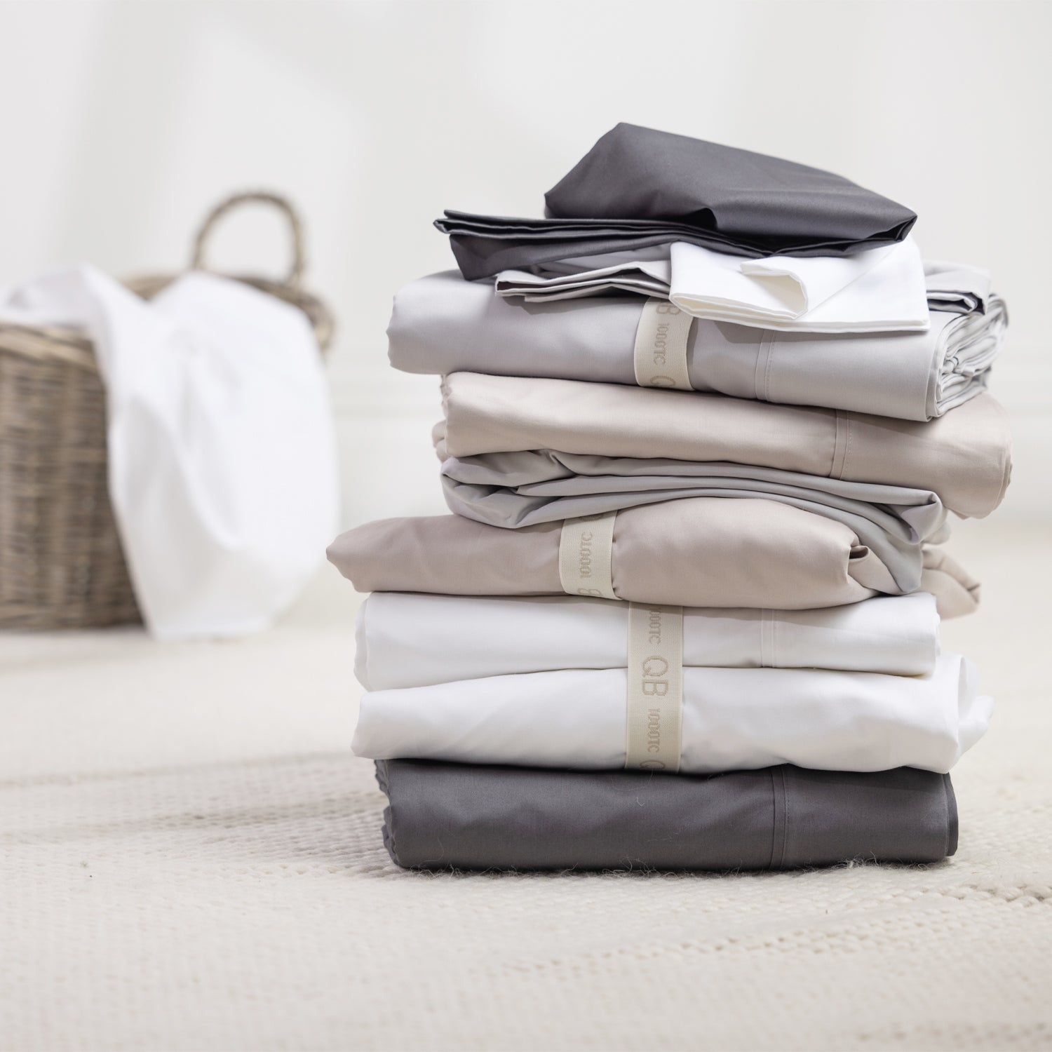 A stack of premium sheets in timeless neutral tones is neatly folded and finished with elegant storage bands, creating a refined and organised linen cupboard aesthetic.