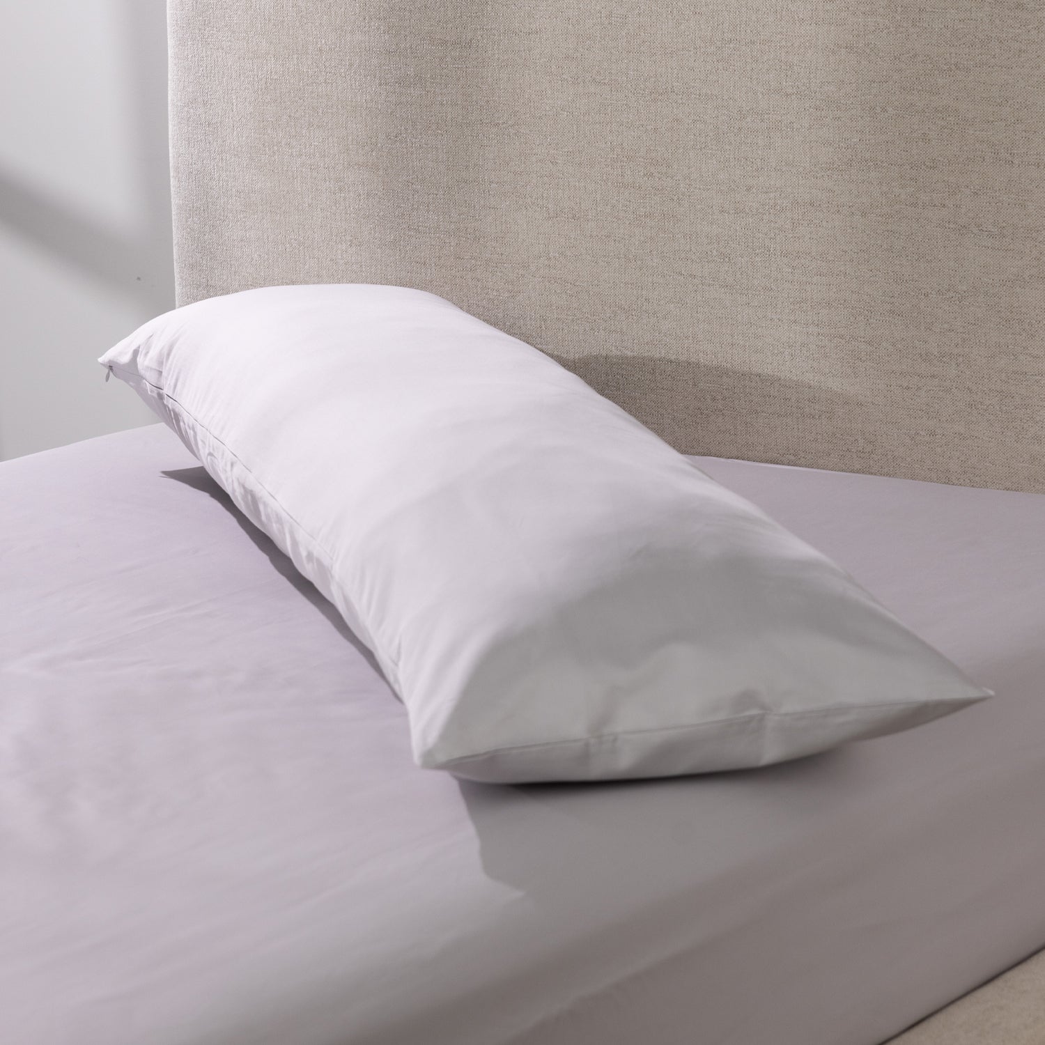 A silver body pillow is dressed in a smooth cotton pillowcase and styled on a neatly made bed, showcasing its clean, luxurious finish and full-length comfort.