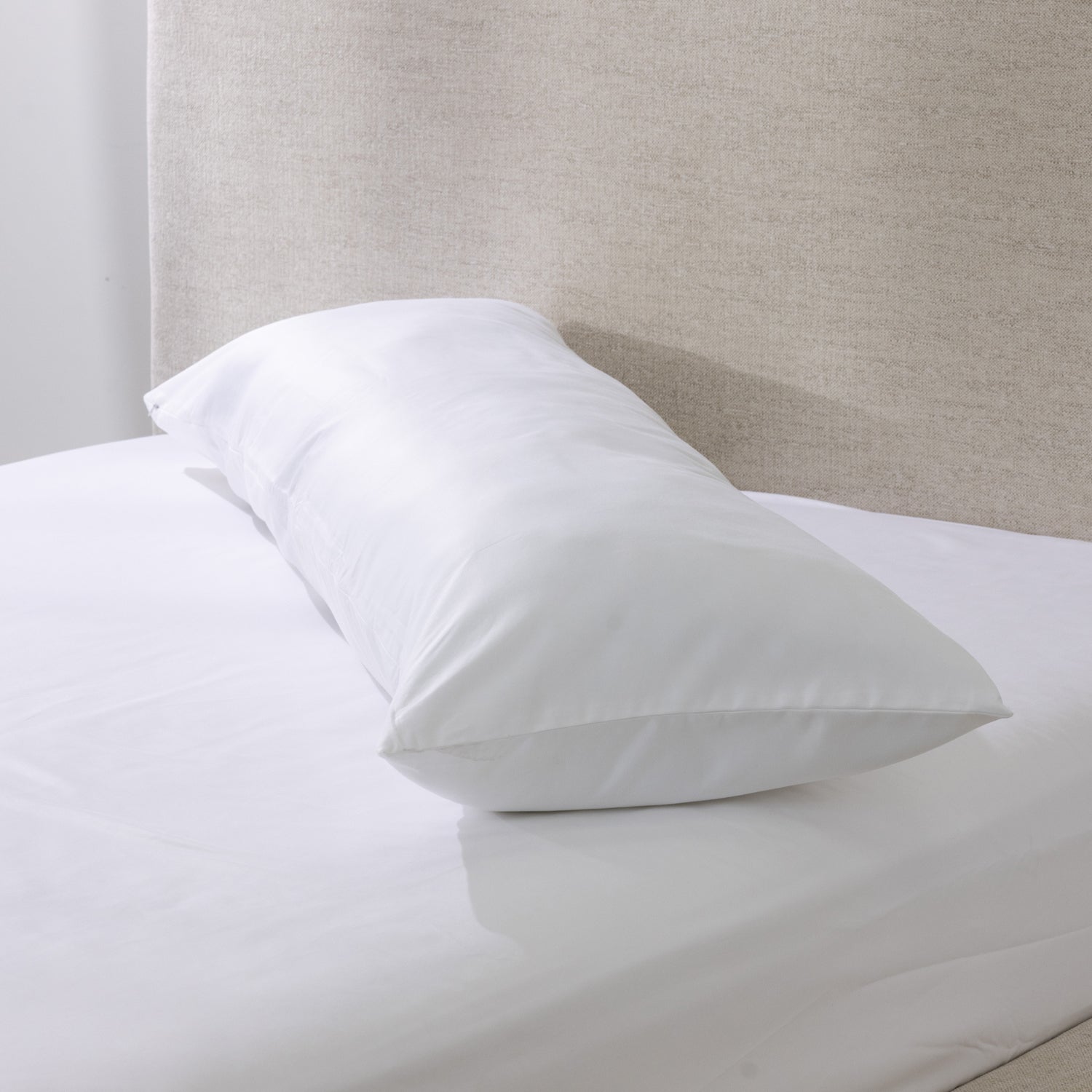 A white body pillow is dressed in a smooth cotton pillowcase and styled on a neatly made bed, showcasing its clean, luxurious finish and full-length comfort.