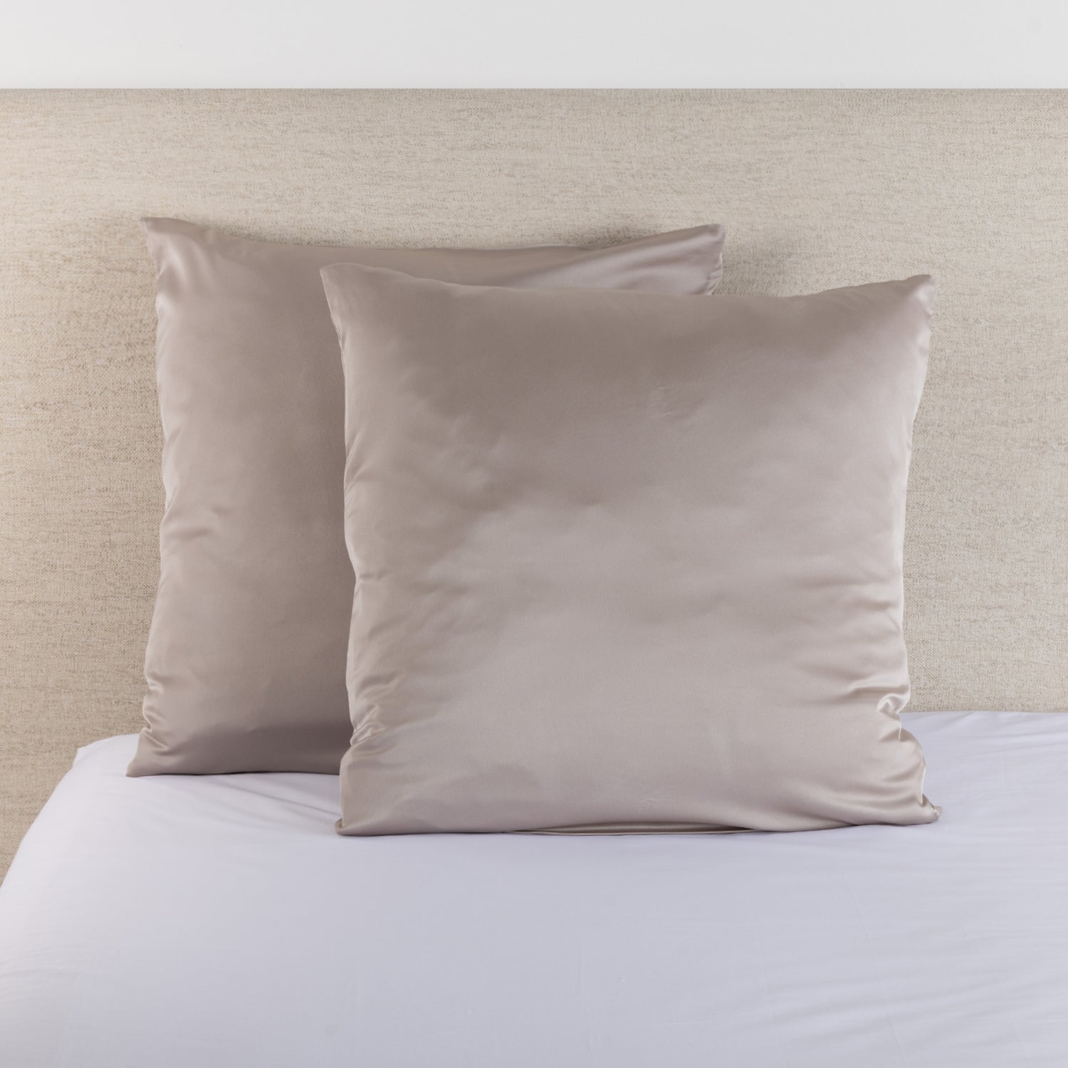 Silver taupe satin Euro pillowcase pair styled on a bed against a neutral upholstered headboard.