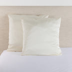 Cream satin Euro pillowcase pair styled on a bed against a neutral upholstered headboard.