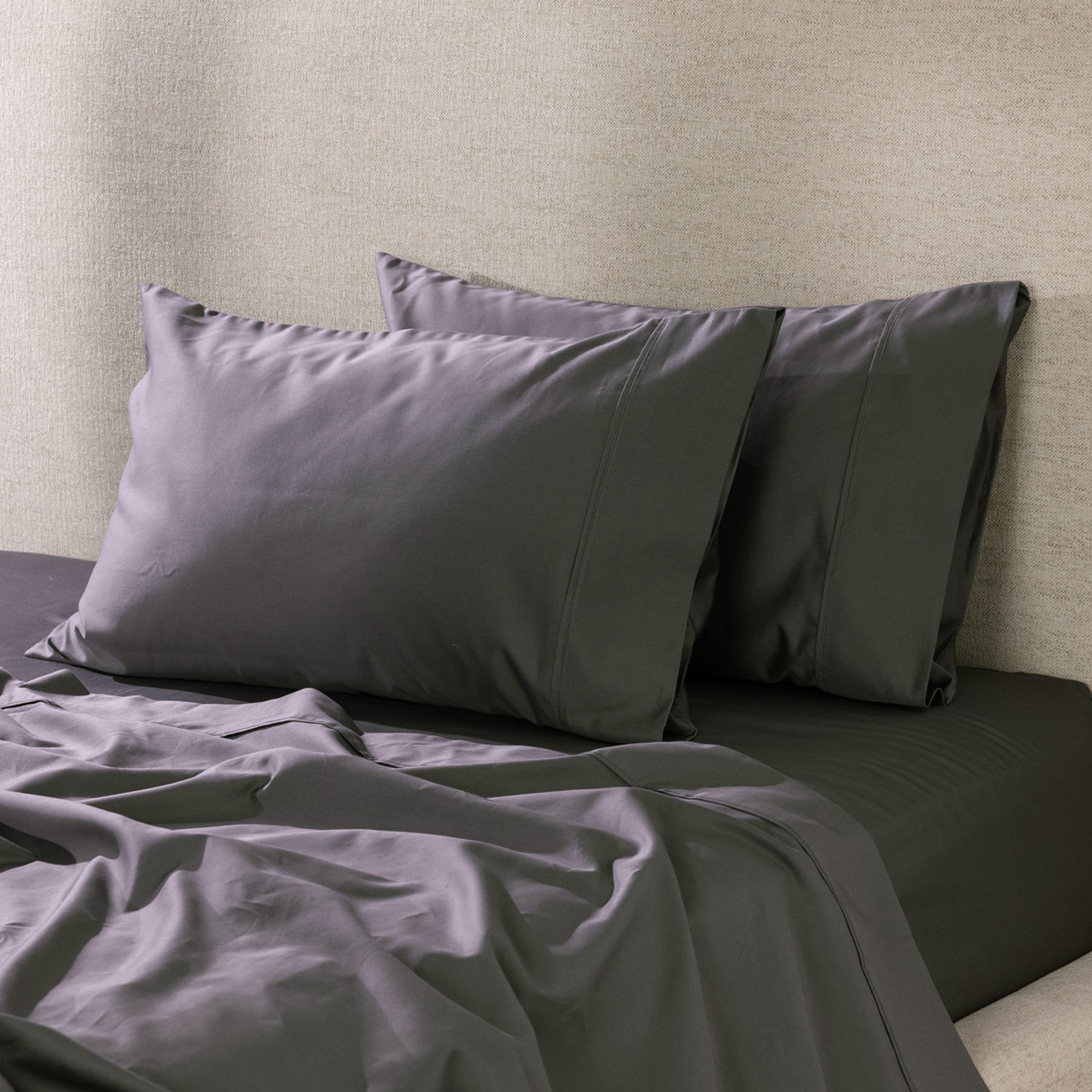 A pair of charcoal pillowcases is beautifully styled on a freshly made bed, showcasing their smooth, luxurious finish and timeless elegance.