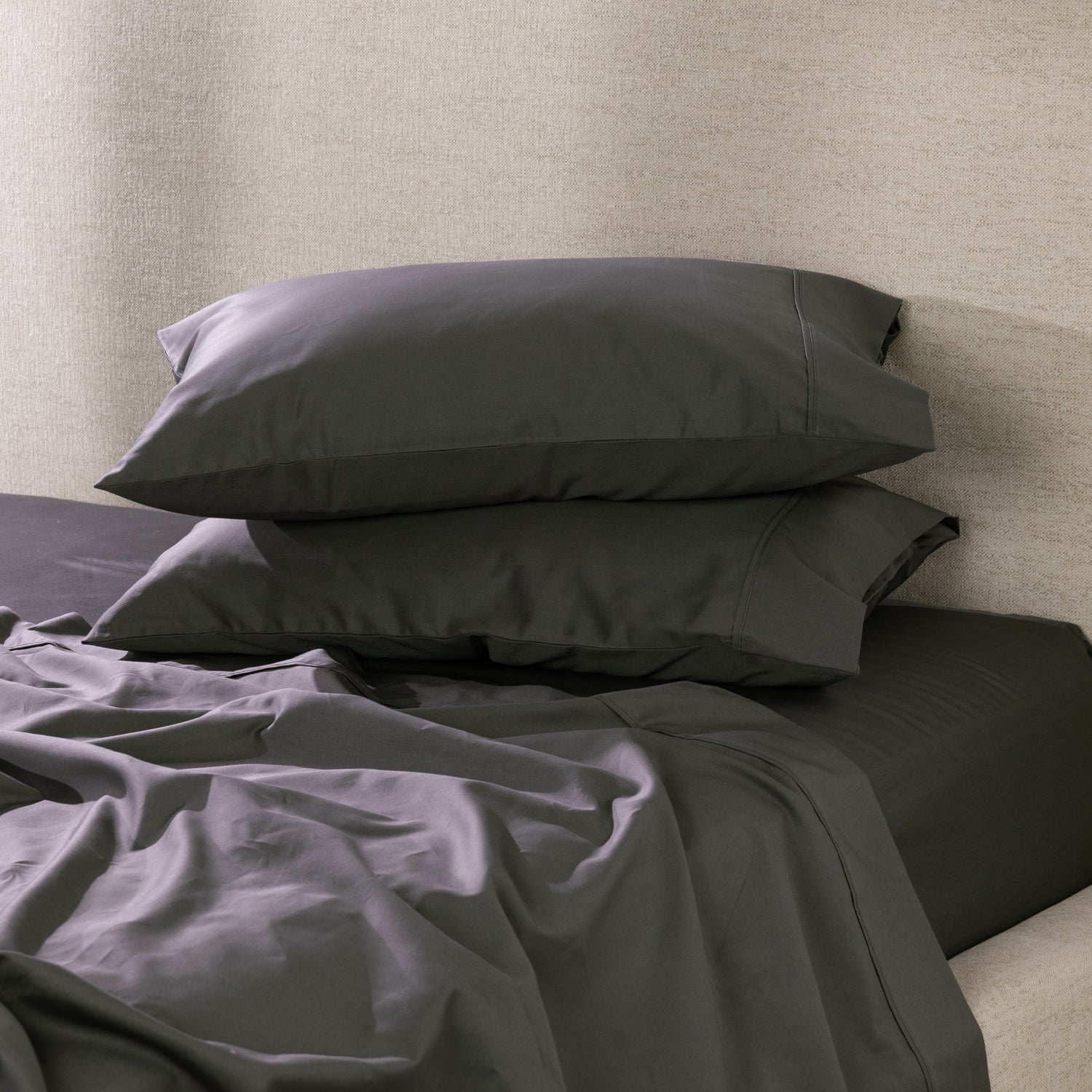 A pair of charcoal pillowcases is beautifully styled on a freshly made bed, showcasing their smooth, luxurious finish and timeless elegance.