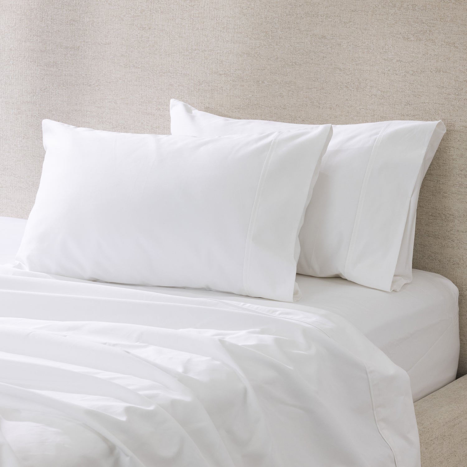 A pair of crisp white pillowcases is beautifully styled on a freshly made bed, showcasing their smooth, luxurious finish and timeless elegance.