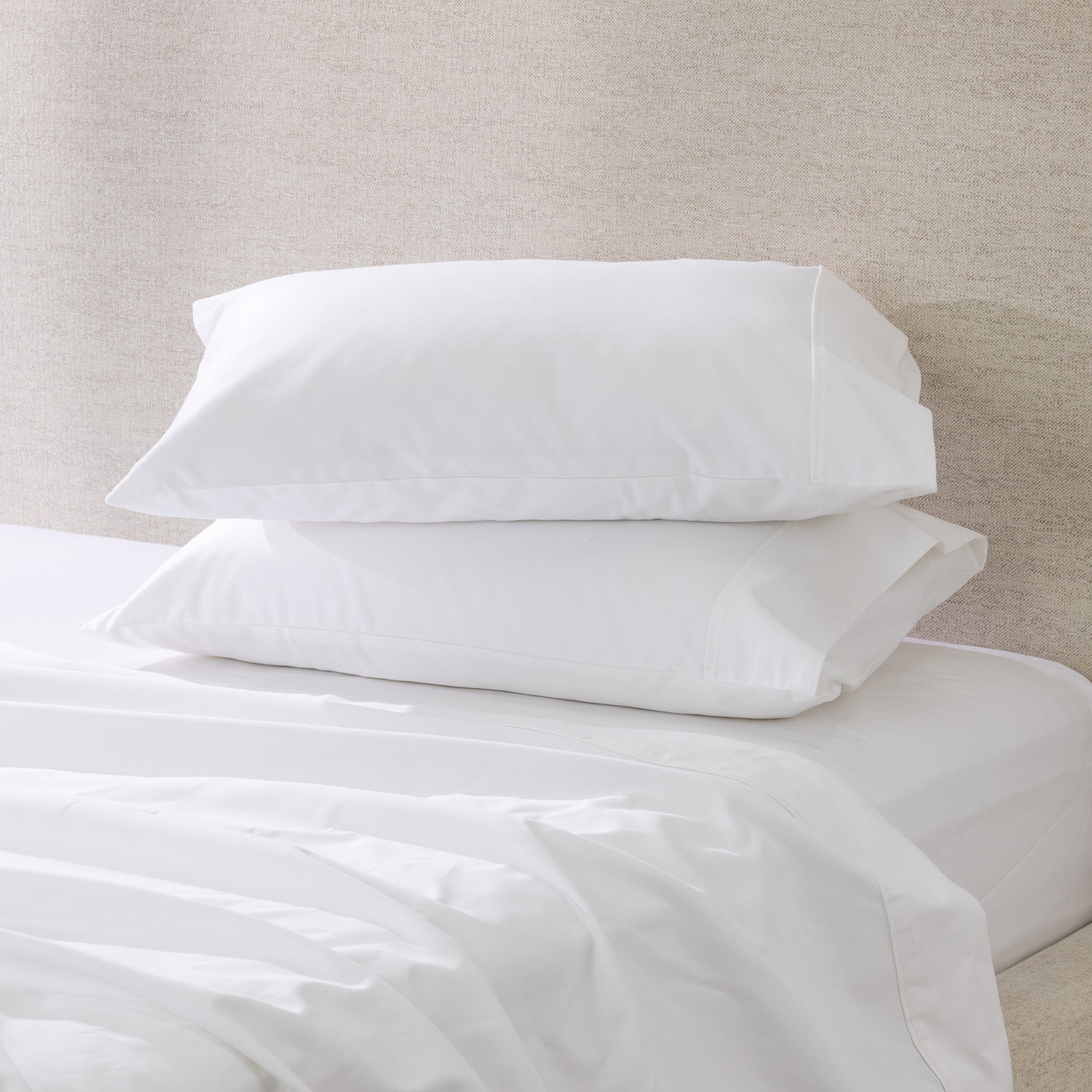 A pair of crisp white pillowcases is beautifully styled on a freshly made bed, showcasing their smooth, luxurious finish and timeless elegance.