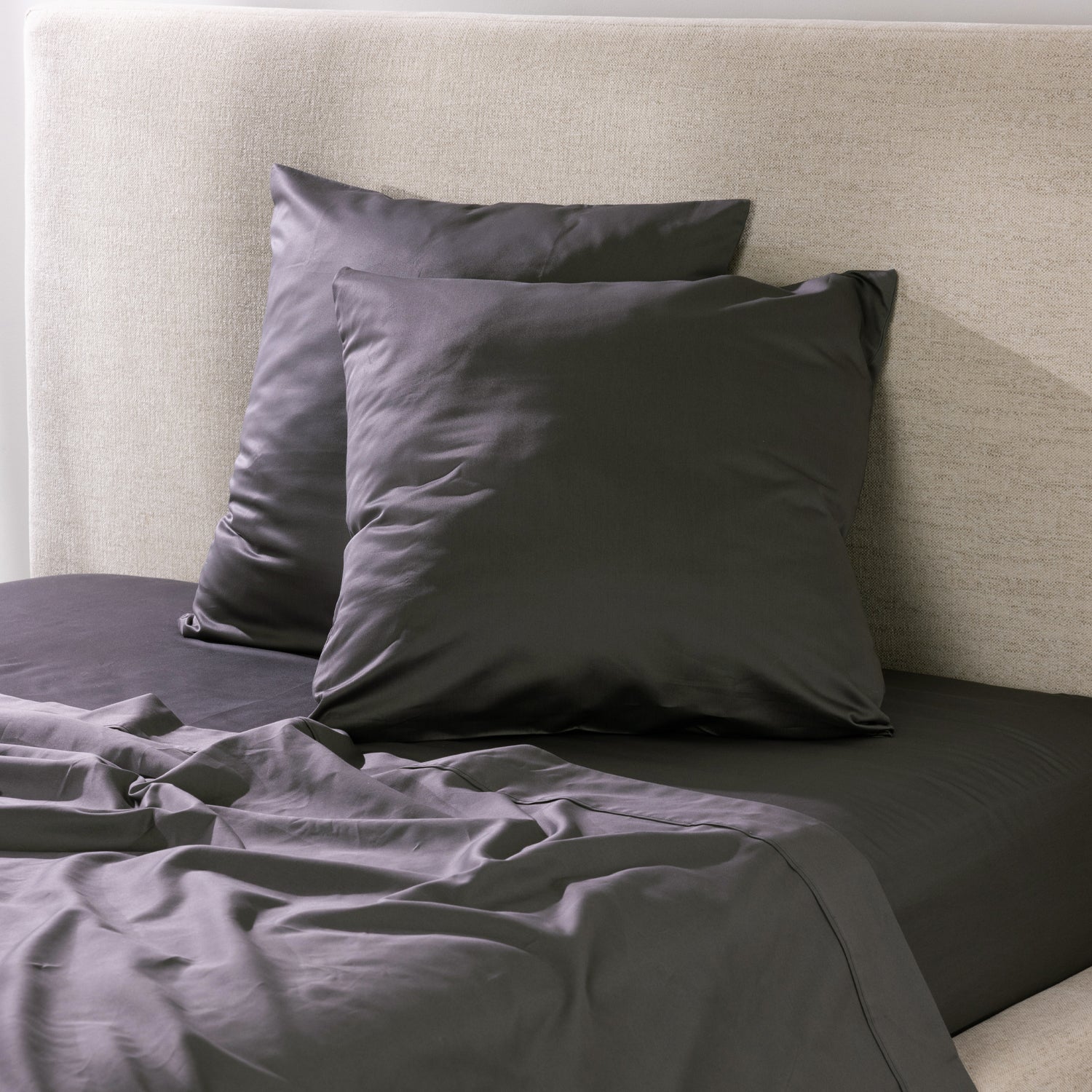 A pair of charcoal European pillowcases is styled on coordinating bedding, creating a sophisticated, contemporary bedroom look with a smooth, luxurious finish.