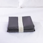 A neatly folded charcoal European pillowcase is secured with a reusable branded storage band, showcasing premium presentation and elegant linen organisation.