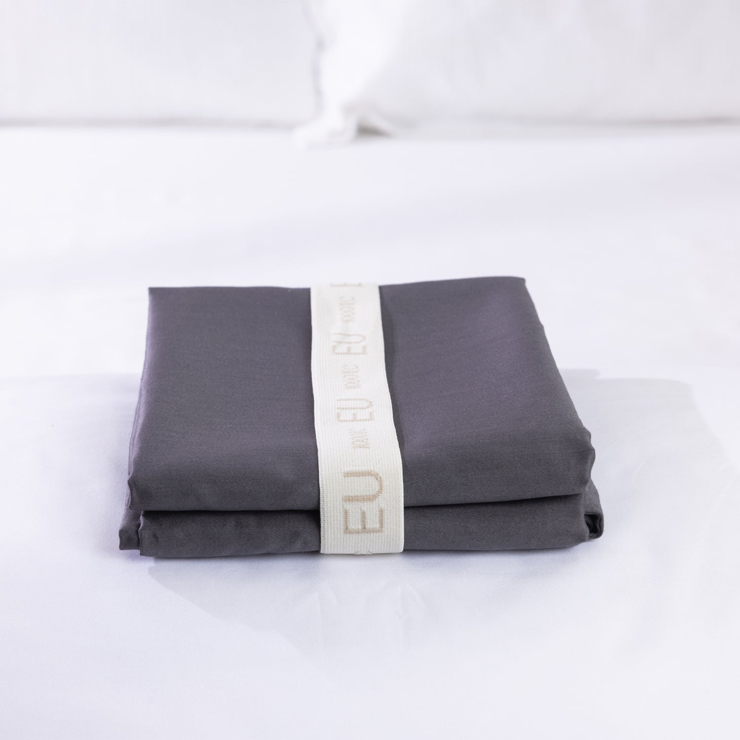 A neatly folded charcoal European pillowcase is secured with a reusable branded storage band, showcasing premium presentation and elegant linen organisation.