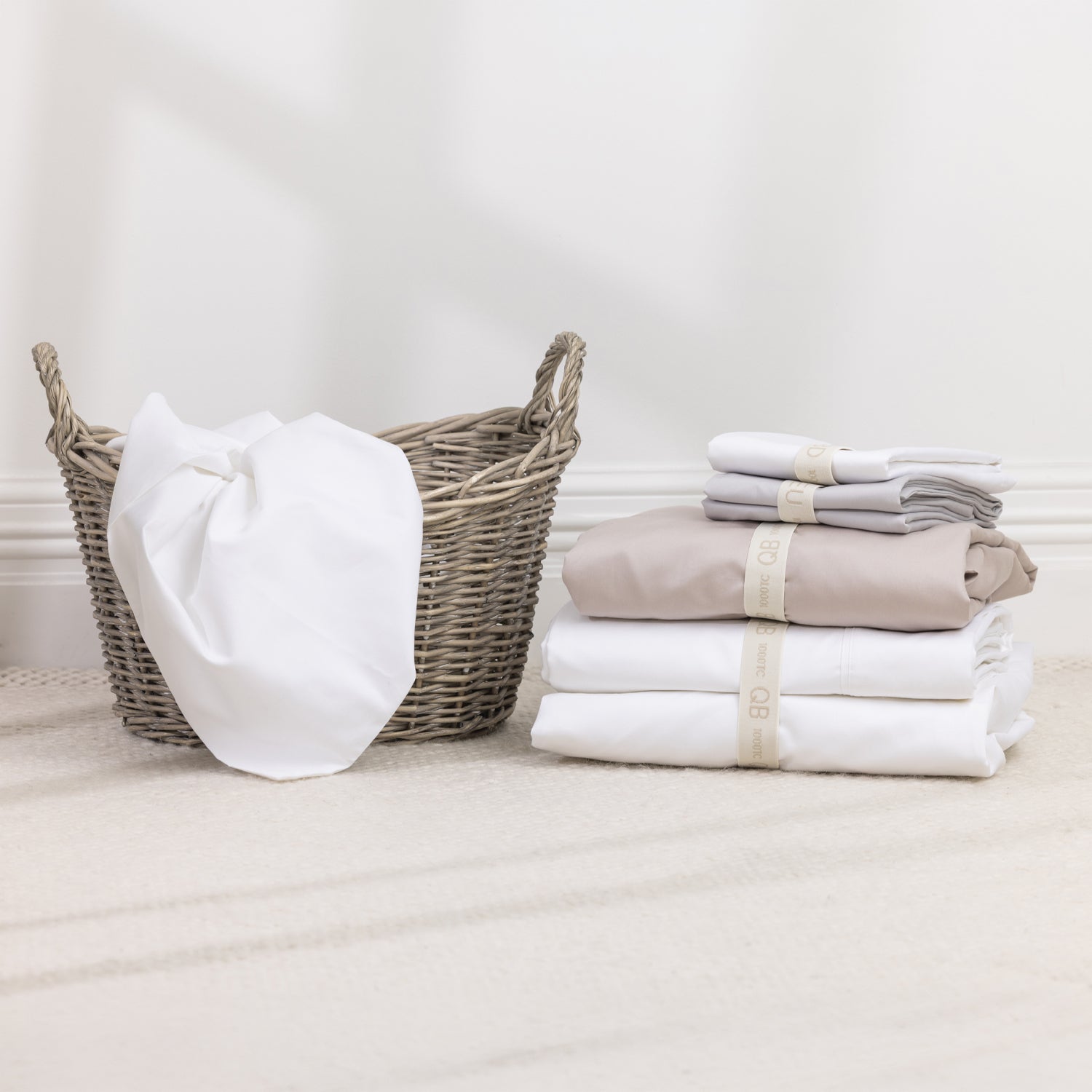 A stack of a premium sheet collection in timeless neutral tones is neatly organised with reusable branded storage bands, bringing elegant style and effortless organisation to your linen cupboard.