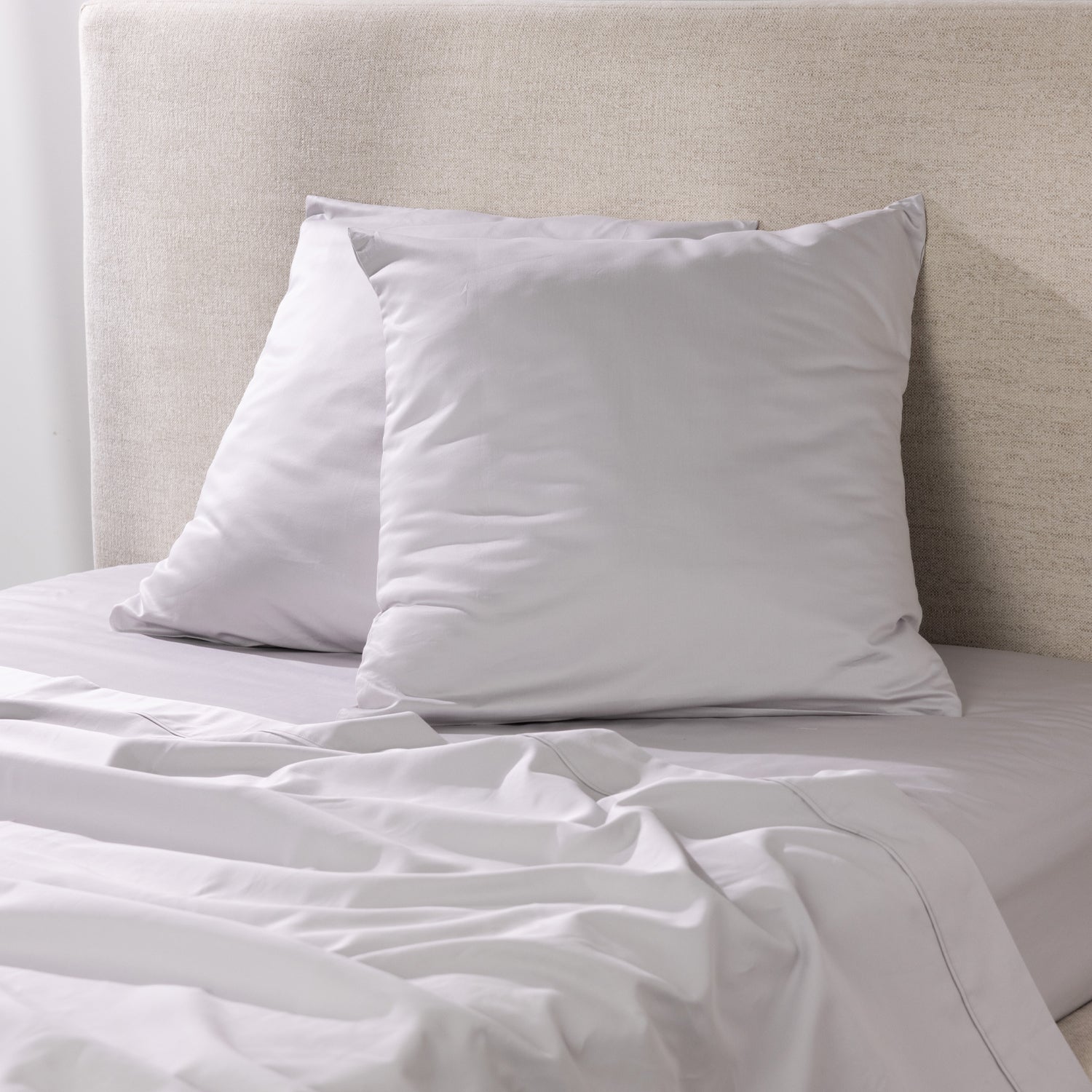 A pair of silver European pillowcases is styled on coordinating bedding, creating a sophisticated, contemporary bedroom look with a smooth, luxurious finish.