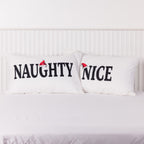 Christmas Wishes Naughty and Nice Pillowcase Pair displayed side by side on a white bed, featuring black lettering and red Santa hats.