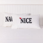 Close-up of the white Christmas Wishes Nice pillowcase featuring bold black lettering and a red Santa hat, displayed in front of the Naughty pillowcase.