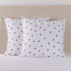 Pure & Simple Monroe European Pillowcase Pair in white with black polka dots, styled on a bed against a neutral upholstered headboard.