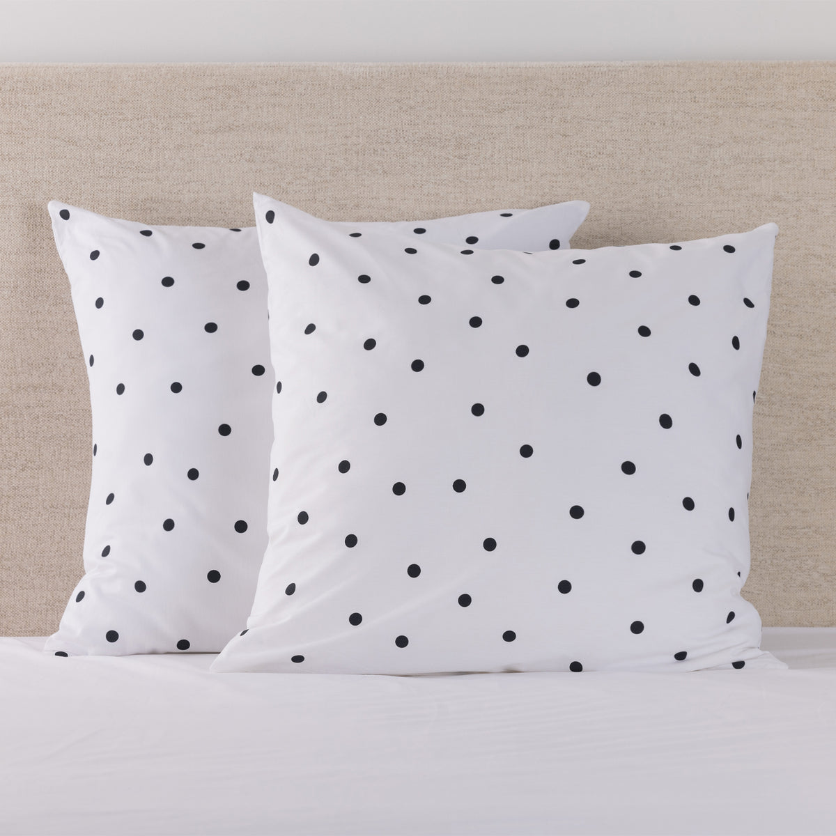 Pure & Simple Monroe European Pillowcase Pair in white with black polka dots, styled on a bed against a neutral upholstered headboard.